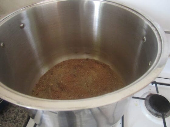 A stainless steel pot with sand sitting on a gas cooker stove